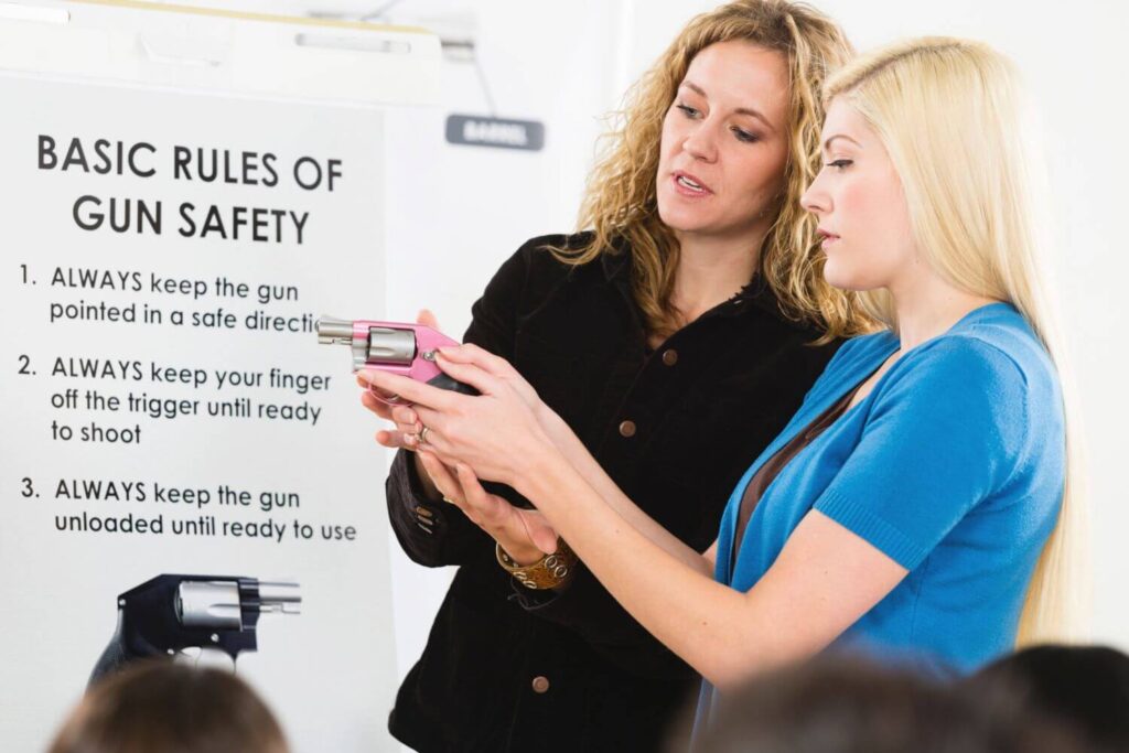 A female firearms instructor is demonstrating proper pistol grip to a female student in a gun safety class