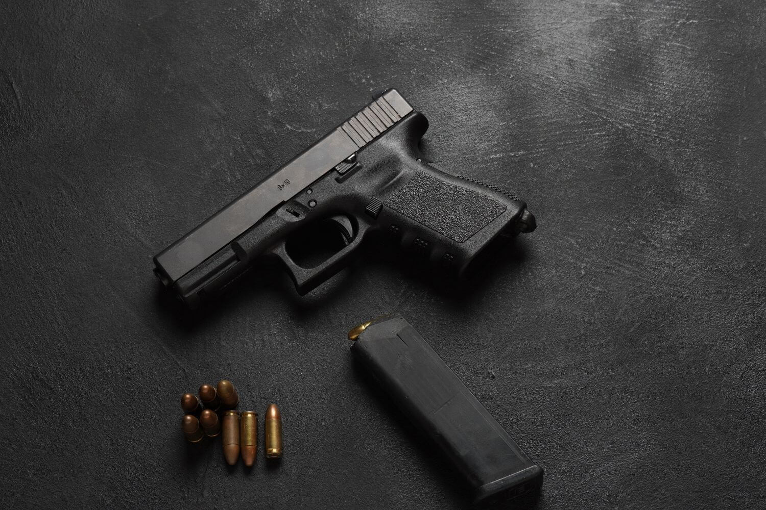 Black gun on a table with magazine and bullets lying next to it.